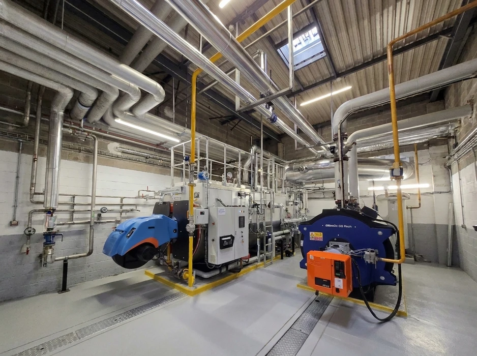 Salle de chaufferie industrielle avec deux chaudières à gaz de grande capacité, équipées de brûleurs (bleu et orange)