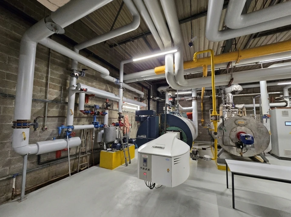 Intérieur industriel moderne avec réseau complexe de tuyauteries métalliques galvanisées, vannes de régulation bleues, réservoir cylindrique jaune et structures de support